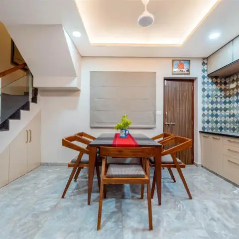 Photo of a dining area tucked under the staircase: a teak table with splayed-leg chairs and a red runner, cream under-stair storage cabinets behind