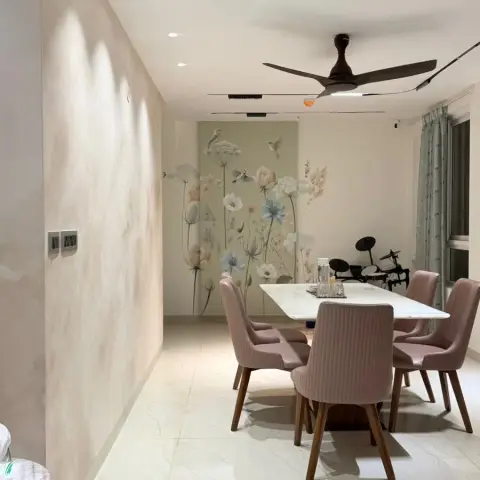 Photo of a dining area where six dusty-pink ribbed chairs on wooden legs surround a white marble-top table against a pastel botanical-and-bird wallpaper mural