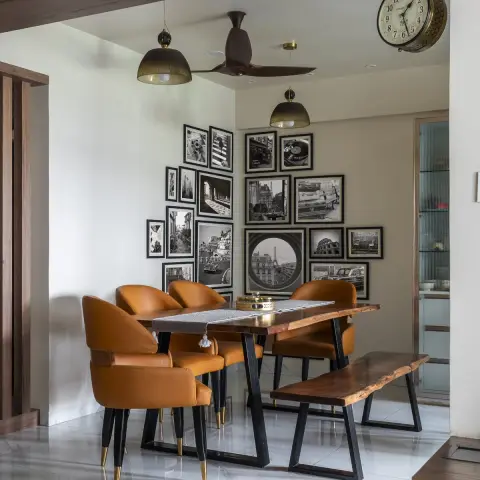 Photo of a dining corner: a live-edge wood table on black trestle legs with tan leather chairs on brass-tipped tapered legs and a matching live-edge bench
