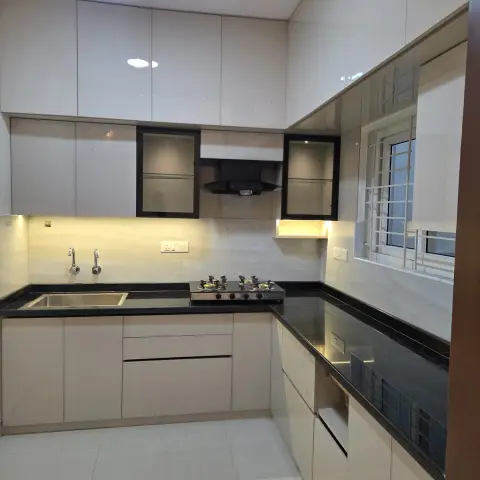 Photo of a just-handed-over ivory high-gloss U-kitchen, still empty — black granite counters with a drop-in steel sink and four-burner hob, marble-look dado