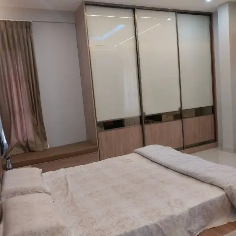 Photo of a lived-in bedroom: a three-shutter sliding wardrobe in cream lacquered glass with a walnut laminate base and bronze mirror band