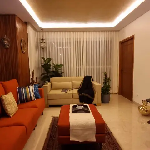 Photo of a lived-in Indian living room with a burnt-orange sofa and matching ottoman on a Persian-style rug