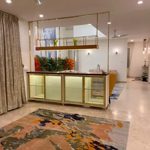 Photo of a living area split by a brass-framed glass display cabinet topped with a wooden shelf and two green vases