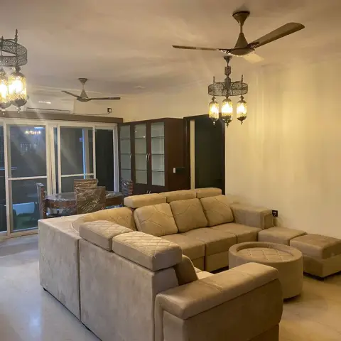 Photo of a living room at night with a beige suede sectional and matching ottomans under two Moroccan filigree chandeliers hung beside the ceiling fans