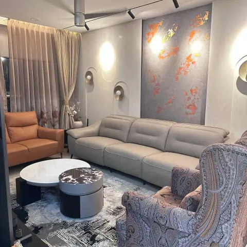 Photo of a living room with a tall orange-and-gold textured art panel above a beige leather recliner sofa, brass disc sconces on the plaster wall