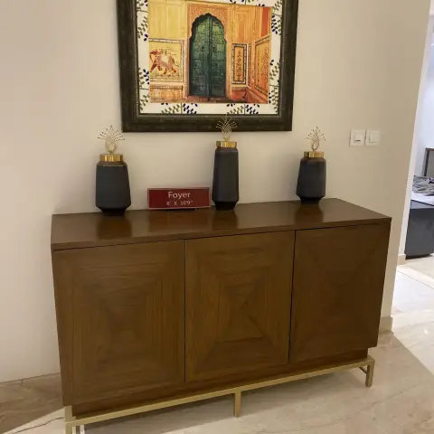 Photo of a show-flat foyer wall: a walnut sideboard with mitred veneer panels on a slim brass frame, three matte black jars with brass lids and fan finials