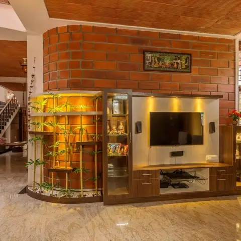 Photo of a South Indian living room built around a curved exposed-brick wall: a veneer TV unit with glazed display cabinets