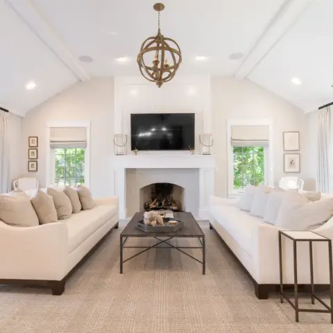 Photo of a vaulted, white-beamed living room with two cream sofas facing each other across a sisal rug and an iron-framed coffee table