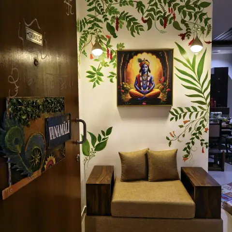 Photo of an apartment entry foyer where a hand-painted foliage mural frames a Krishna painting, two brass bell pendants hang either side