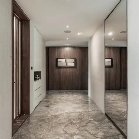 Photo of an entrance foyer where a dark walnut main door with a slim glazed strip faces a frameless full-height mirror panel