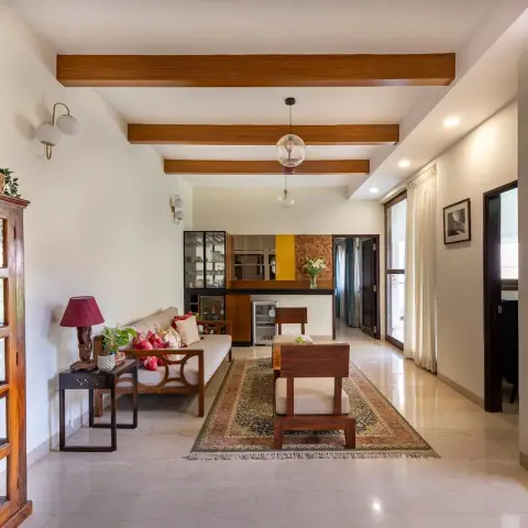 Photograph of a beamed living room in a two-level home: teak sofa and armchairs on a faded kilim rug