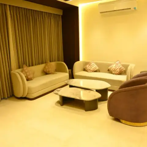 Photograph of a drawing room where two curved cream sofas face a pair of brown velvet swivel tub chairs on brass bases