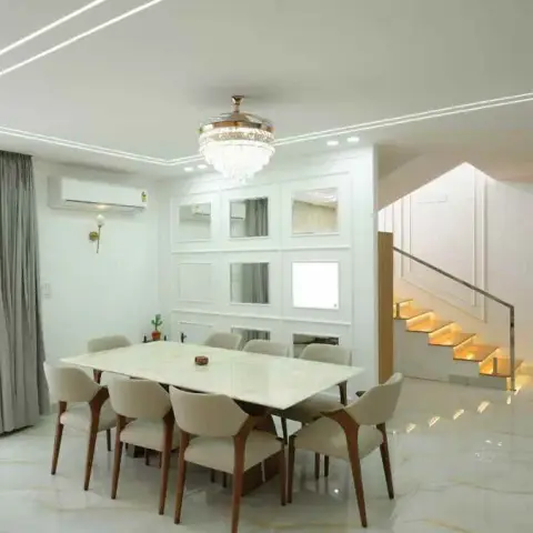 Photograph of an eight-seater dining zone in a tall villa hall - marble-top table under a crystal chandelier with retractable fan blades