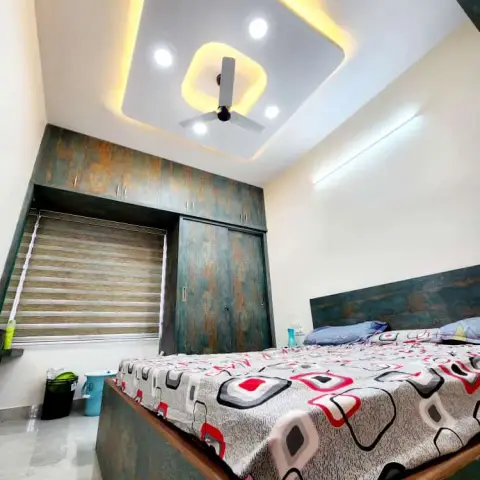 Photograph taken from the bed corner of a bedroom whose teal-and-rust distressed laminate wardrobe with sliding shutters and loft flanks a zebra-blinded