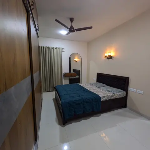 Plain-ceilinged bedroom with a dark basket-weave wooden headboard under a twin amber wall sconce, teal quilt on the bed