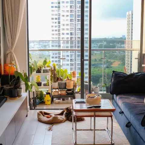 Plant-filled high-rise living room with a navy blue sofa, a glass-and-wood coffee table, a TV console lined with potted plants