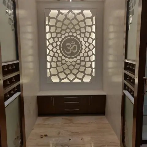 Pooja alcove with a backlit CNC-cut jaali panel featuring an Om motif above a wood-and-marble cabinet, flanked by mirrored wardrobe doors with hanging bells.