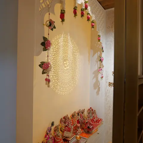 Pooja alcove with a backlit CNC-cut Om mandala wall panel inside an arched jaali frame, fresh flower toranas hanging on either side