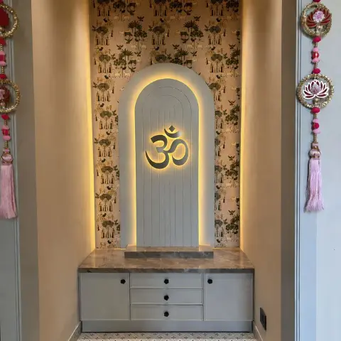 Pooja alcove with a fluted ivory arch carrying a backlit black Om against gold-and-black folk-print wallpaper