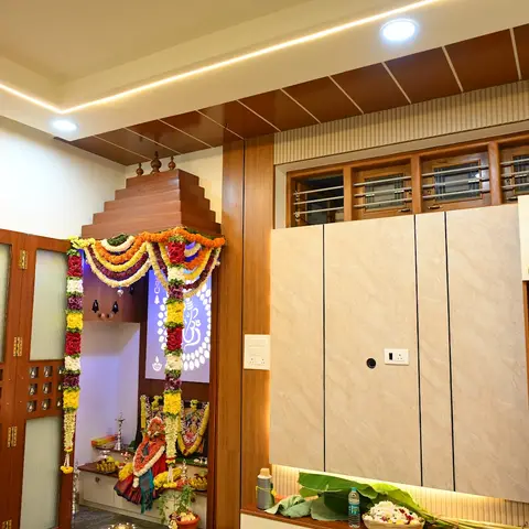 Pooja alcove with a stepped wood temple-tower pediment over the shrine, decorated with fresh flower garlands