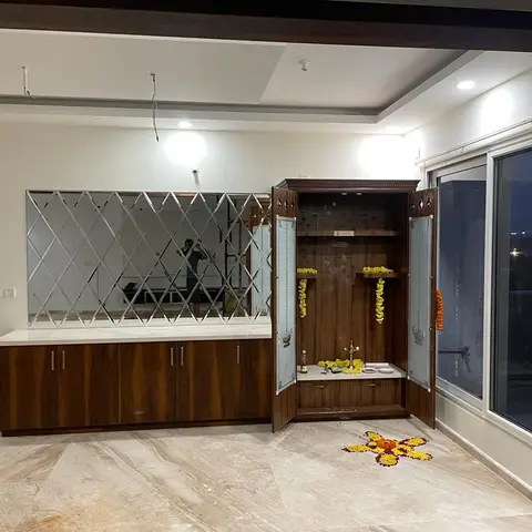 Pooja cabinet with carved wood crown and glass doors open to reveal marigold garlands and a lit oil lamp