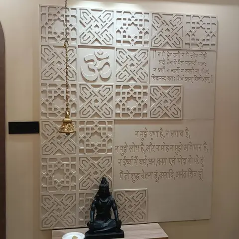Pooja corner with a carved sandstone jaali feature wall bearing an Om motif and Sanskrit verses, a brass hanging bell