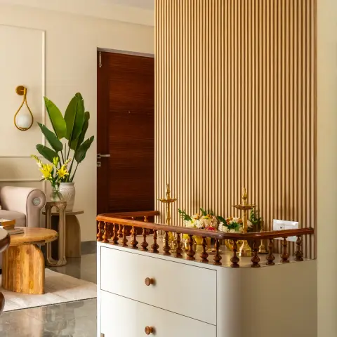 Pooja counter at the edge of a living room: a curved ivory two-drawer plinth topped by a turned-teak balustrade rail