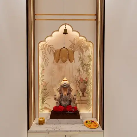 Pooja niche with a scalloped gold-trimmed arch, a botanical mural backdrop, a hanging brass bell and lotus-shaped fixture