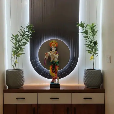 Pooja nook where a Krishna idol stands in a routed circular niche cut into a backlit dark fluted panel