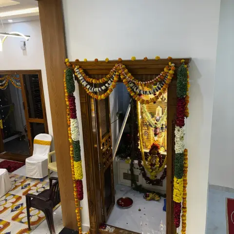 Pooja room doorway dressed in marigold and mango-leaf garlands for a housewarming