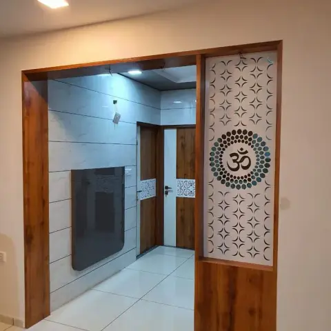 Pooja room entrance framed in wood with a perforated jaali screen bearing an Om motif, opening to a marble-clad mandir chamber