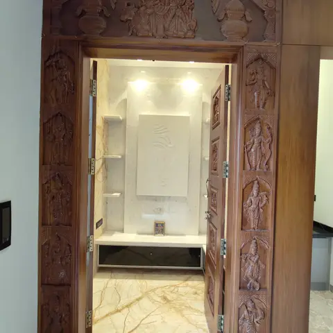 Pooja room entrance with an elaborately carved wood door depicting deities on the frame and panels