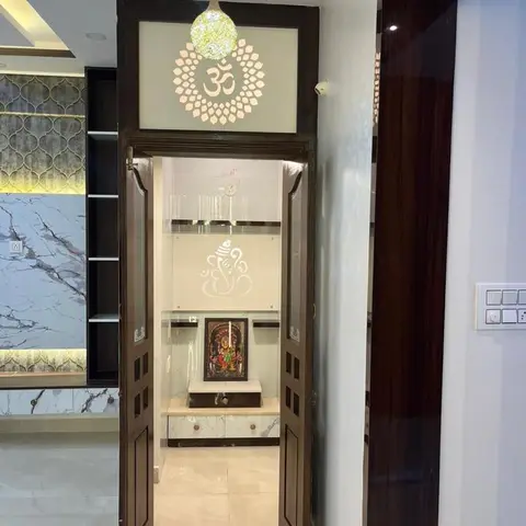 Pooja room framed by a dark wood double door with a backlit Om motif, opening to a white marble unit with a deity silhouette panel.