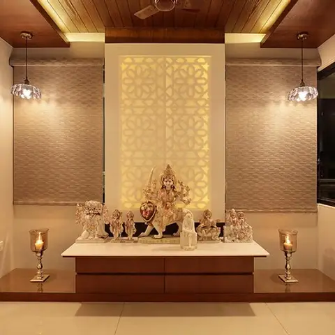 Pooja room with a backlit jaali panel behind the deity idols, flanked by crystal pendant lights under a wood-plank cove ceiling.