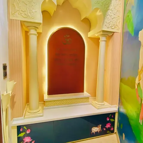 Pooja room with a lotus-crown arched shrine flanked by fluted white pillars, a backlit maroon panel inscribed with Om and Sanskrit verses