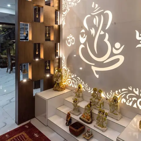 Pooja unit with a backlit CNC-cut Ganesh motif wall panel, a tiered white idol platform, and a wooden partition strung with brass bells.