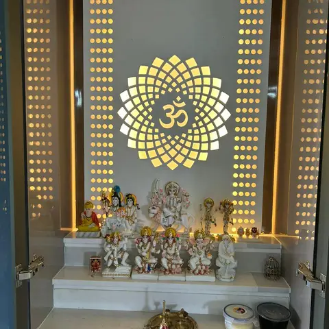 Pooja unit with a backlit lotus-and-Om medallion feature panel, perforated jaali side panels, and a tiered marble platform holding an array of deity idols.