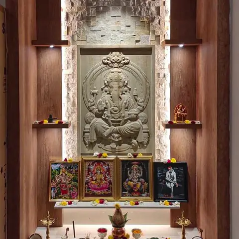 Pooja unit with a carved stone Ganesha relief panel framed in wood joinery over a marble offering counter.
