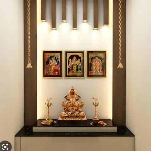 Pooja unit with a fluted wood surround, brass hanging bells, a gold Ganesh idol, and a black granite platform over closed cabinet storage