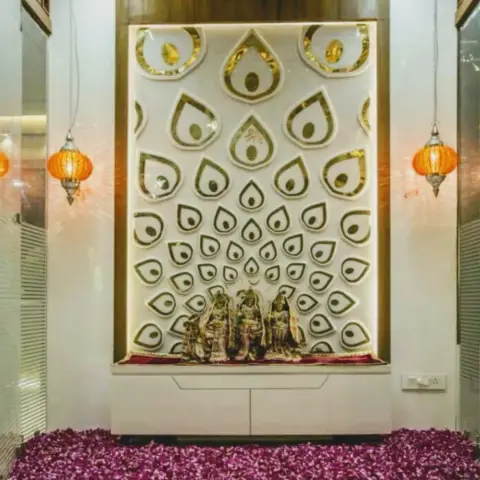 Pooja unit with a gold and white teardrop-motif 3D wall panel backdrop, deity idols on a marble ledge and hanging Moroccan-style lanterns on either side