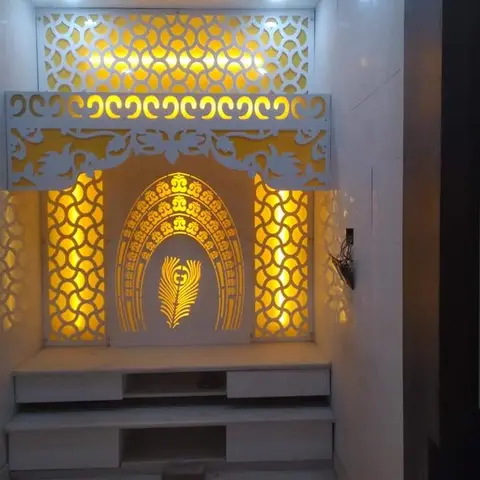 Pooja unit with an ornate white CNC-cut jaali backdrop, a backlit peacock-feather and Om motif, and a marble-look base with drawer storage.