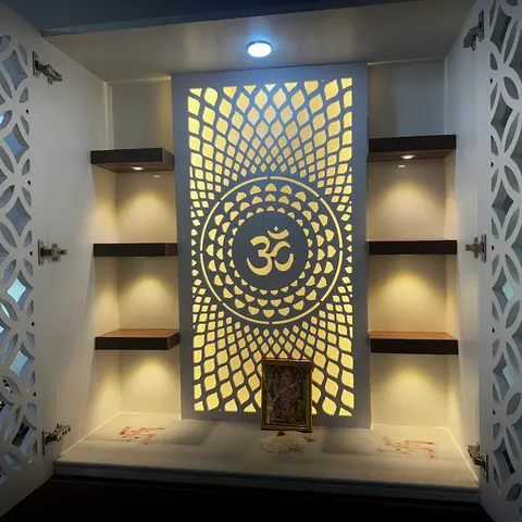 Pooja unit with CNC-cut jaali cabinet doors and a backlit Om-motif jaali feature panel above a marble shelf holding a deity frame
