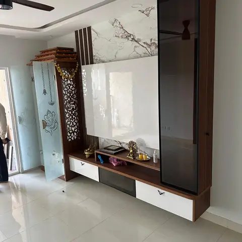 Pooja unit with etched glass doors featuring a Ganesh motif, bells and torans, beside a marble-backed console.