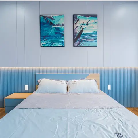 Powder-blue bedroom where a flat panelled upper wall meets a fluted blue dado, two turquoise abstract canvases hang over the oak-topped headboard and a lit oak