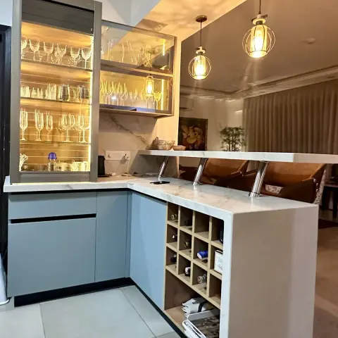 Powder-blue handleless base units turning into a white marble-topped breakfast peninsula with a grid wine rack in its return, under two caged-globe pendants