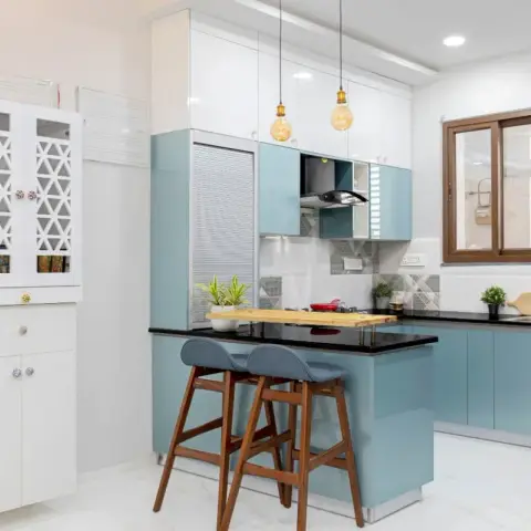 Powder-blue high-gloss kitchen with a peninsula breakfast counter and two wooden bar stools, Edison pendants over the black granite top