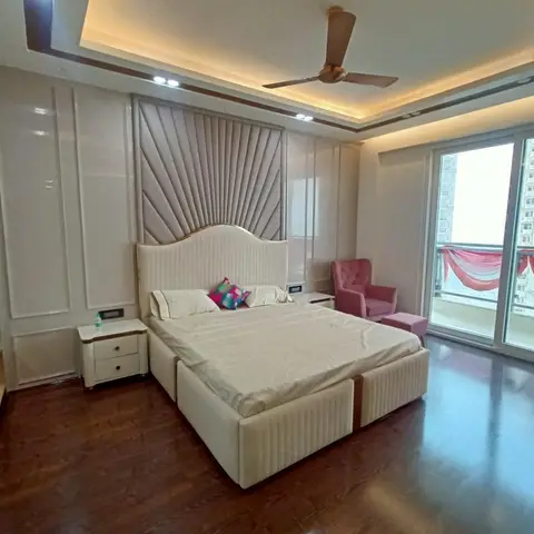 Primary bedroom with a sunburst-textured upholstered headboard wall, glossy wardrobe, and floor-to-ceiling balcony doors overlooking the city skyline.