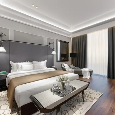 Primary bedroom with a tall grey channel-striped headboard flanked by swing-arm sconces, a patterned bench with breakfast tray at the foot of the bed