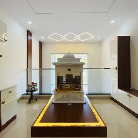 Raised pooja platform with a carved white marble-finish mandir backlit with warm LED strip lighting under a glass railing