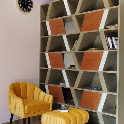 Reading corner with a geometric asymmetric bookshelf in orange and taupe, a mustard velvet channel-tufted armchair and matching ottoman